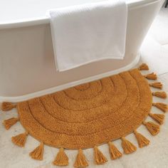 a bathroom rug with tassels on the floor next to a white bath tub