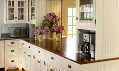 a kitchen with white cabinets and wooden counter tops, flowers in vases on the island