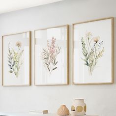 three framed art prints on the wall above a table with vases and books in front of them