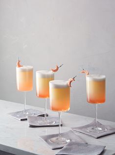 three glasses filled with drinks sitting on top of a white counter next to silver napkins