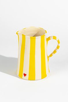 a yellow and white striped pitcher with a red heart on the side, against a white background