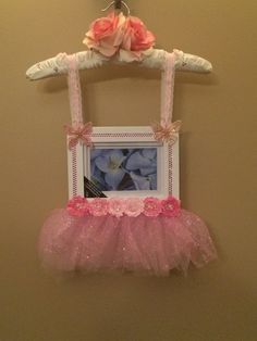 a pink tutu skirt hanging on a wall next to a framed photo with flowers