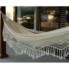 a large white hammock hanging from a wooden pole on a porch with windows in the background