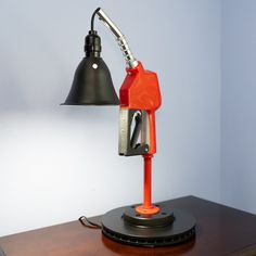 an orange gas pump sitting on top of a wooden table next to a black lamp