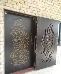 two metal doors with designs on them in front of a brick wall and door frame