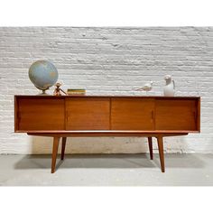 a wooden sideboard with two drawers and a globe on top, in front of a white brick wall