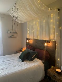 a bed with white sheets and lights on the headboard is in front of a window