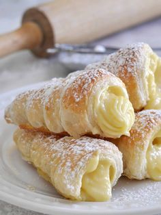 three pastries sitting on top of a white plate covered in powdered sugar and icing