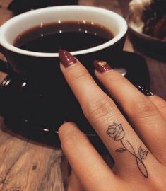 a woman's hand with a small rose tattoo on her left finger next to a cup of coffee