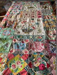 an old quilt is laying on top of a table with flowers and other things around it