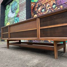 a wooden bench sitting in front of a building with graffiti on the wall behind it