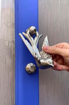 a person is holding a metal bird door knocker on a blue and gray door