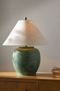 a green lamp sitting on top of a wooden table next to a basket and bottle