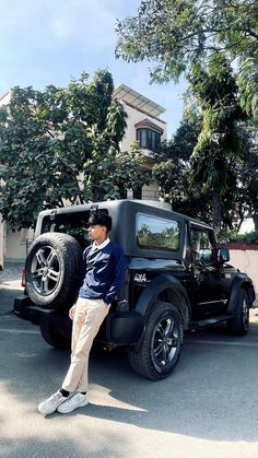 a man sitting on the back of a black jeep parked in front of a house