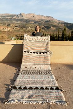 a woman sitting on top of a blanket in the middle of a desert area with mountains in the background