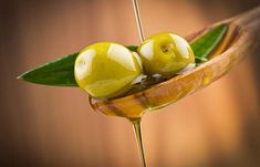 two green olives sitting on top of a wooden spoon covered in melted liquid and leaves