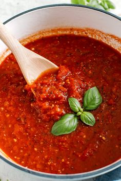 a wooden spoon in a pot filled with tomato sauce and basil leaves on the side