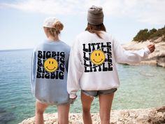 two girls wearing sweatshirts with smiley faces on them looking out at the water and cliffs