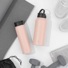 two pink water bottles sitting on top of a white table next to gray dumbbells