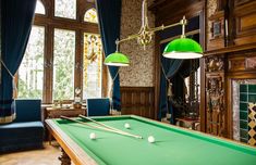 a pool table with two green lamps hanging from it's sides in front of a fireplace