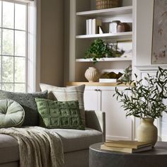 a living room filled with furniture next to a window covered in green and white pillows