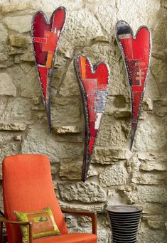 two red heart shaped metal wall hangings on a stone wall next to an orange chair