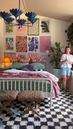 a woman standing next to a bed in a room with lots of pictures on the wall