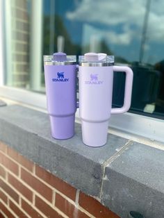 two purple coffee mugs sitting on top of a window sill next to a brick wall