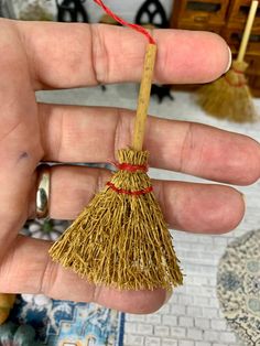 a hand holding a small broom with a red string on it's end, in front of a table