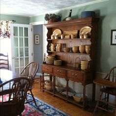 a dining room table and chairs in front of a hutch with dishes on it