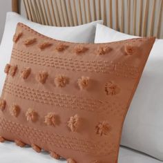 an orange pillow with pom - poms on it sitting on top of a bed