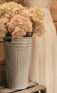 a white vase filled with pink flowers on top of a wooden table next to a dress