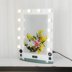 a mirror that has some lights on it with flowers in the reflection and light bulbs behind it