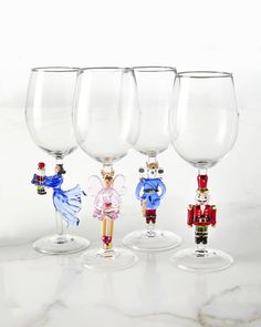 four wine glasses with figurines in them on a marble counter top, one is holding a toy soldier and the other has a nutcracker figure