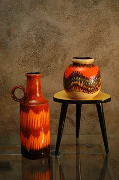 two vases sitting on top of a table next to each other in front of a wall