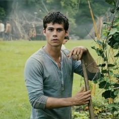 a young man holding a stick in front of a bush with other people behind him