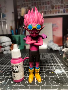 a pink doll with sunglasses and yellow boots next to a bottle of glue on a table