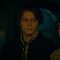 a young man and woman standing next to each other in a dark room with the lights on