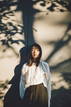 a woman standing in front of a tree with her shadow on the wall behind her