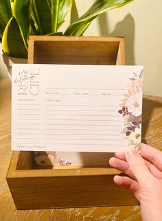 a hand holding a notepad in a wooden box next to a potted plant