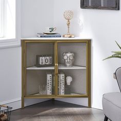 a white and gold cabinet with books on it next to a gray chair in front of a window