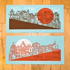 two cards with buildings on them sitting next to each other in front of a wooden floor