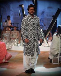 a man is walking down the runway wearing an ethnic outfit and standing in front of other people