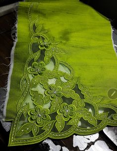 a green piece of cloth with an intricate design on the front and back side, sitting on a table