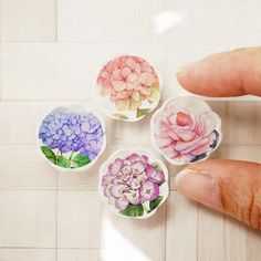 four small flowers are placed in bowls on the floor, one being held by a person's hand