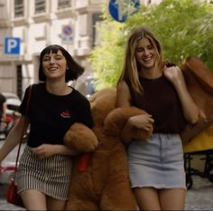 two women walking down the street with large teddy bears