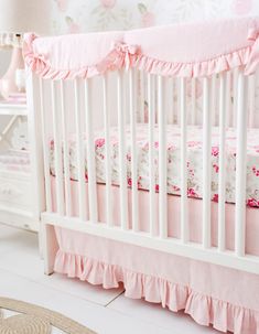 a white crib with pink bedding and floral wallpaper