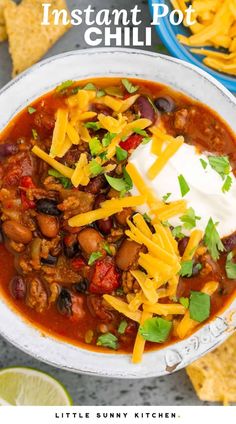 a white bowl filled with chili and cheese next to tortilla chips on the side