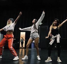 three young women are performing on stage with their arms in the air