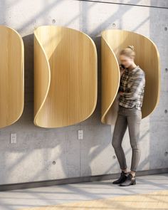 a woman standing in front of three wooden wall mounted urinals, talking on her cell phone